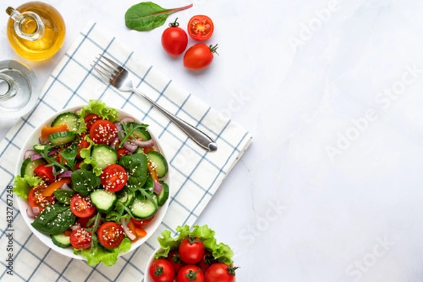 Obraz Salad made with pieces of tomatoes, cucumbers, onion, bell pepper slices, arugula, sesame, basil and dressed with olive oil. Healthy food concept, a vegetarian diet. Copy space, empty place for text.