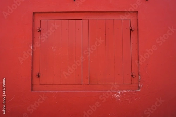 Fototapeta Pair of matching wooden panel window shutters framed in matching bright red horizontal wall