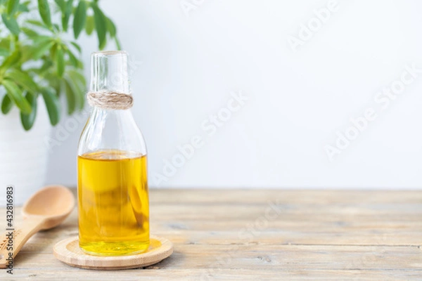 Fototapeta Olive oil in a bottle, a spoon and a flower in a pot on a wooden table on a white background. Copy space.