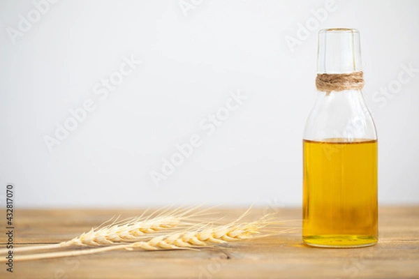 Fototapeta Oil from wheat in a bottle and wheat ears on a wooden table on a white background. Copy space.