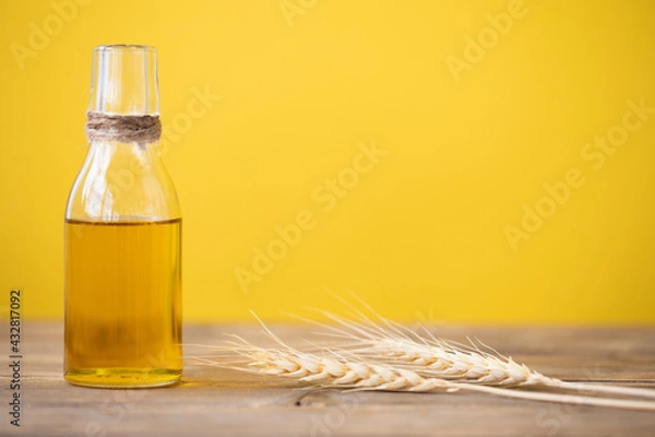 Fototapeta Oil from wheat in a bottle and wheat ears on a wooden table on a yellow background. Copy space.