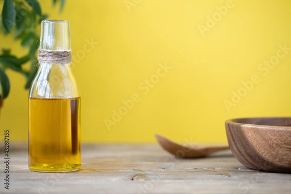 Fototapeta Olive oil in a bottle, a spoon, a plate and a flower in a pot on a wooden table on a yellow background. Copy space.