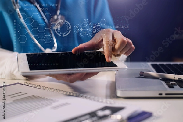 Fototapeta Doctor working on laptop computer and tablet and medical stethoscope on clipboard on desk.