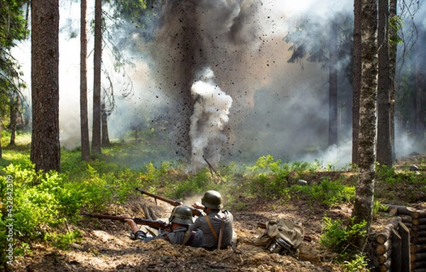 Fototapeta Finnish soldiers in World War II uniforms are fighting from a trench, with a shell explosion in the background.