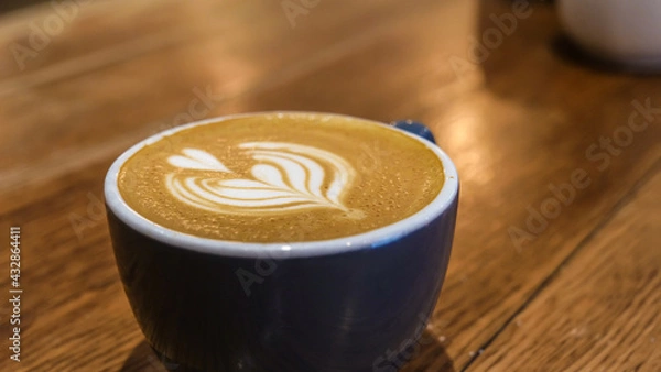 Fototapeta A Blue coffee cup with a steamed milk leaf, Placed on a wooden counter in a cafe. Coffee Art.