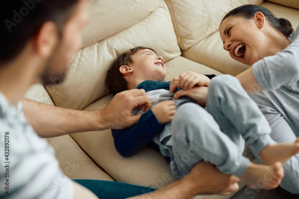Fototapeta Joyful parents tickling their son and enjoying in family time at home.