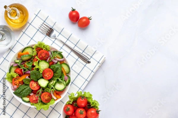 Obraz Vegetables on a white plate on a gray marble background. Top view. Salad made with cherry tomatoes, cucumbers, arugula, basil and dressed with olive oil. Healthy food concept, a vegan diet. Copy space