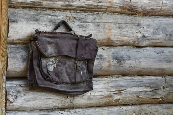Fototapeta An antique leather bag hangs on a log wall. Dirty, shabby brown 