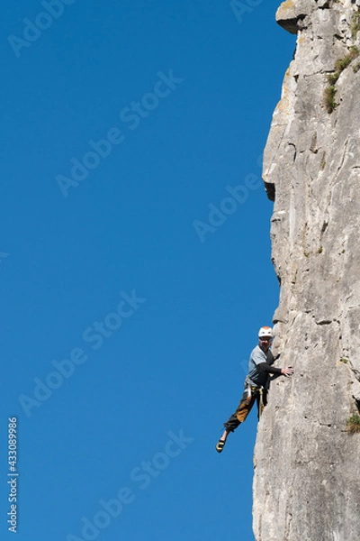 Obraz Climber poses throwing his leg into the void during rock climbing.