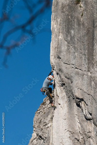 Obraz Male athlete climbs gray wall with blue sky in the background.
