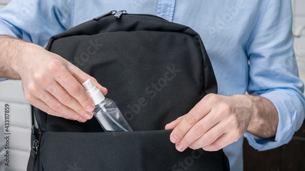 Obraz Man puts sanitizer or antiseptic,  in a backpack, male hands, cropped image, close-up