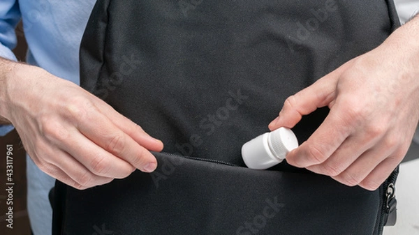 Obraz Man puts container of pill in a backpack, male hands, cropped image, close-up