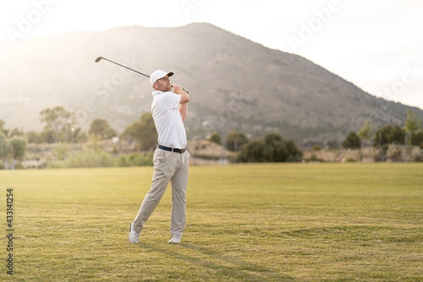 Fototapeta Golf player making a perfect swing on the golf course in the sunset.