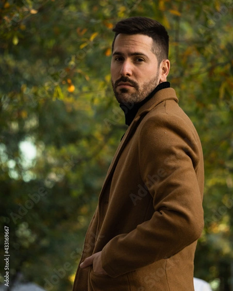 Fototapeta Fall portrait of a bearded man with a brown coat at sunset time in the park