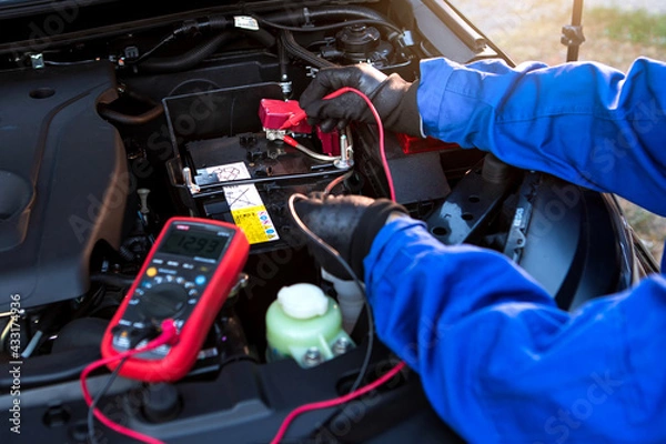 Fototapeta Technician uses multimeter voltmeter to check voltage level in car battery. Service and Maintenance car battery.