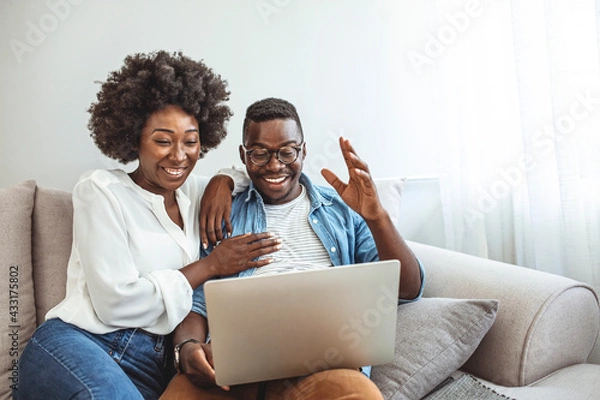 Obraz Young couple sitting in their living room with laptop waving to their marital therapist after successful online therapy and saved marriage. Shot of a smiling young couple using a laptop while relaxing