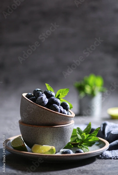 Fototapeta Fresh berries with drops, blueberries with lime, mint in a bowl on a gray background. Summer, freshness, sunshine. Background image, copy space