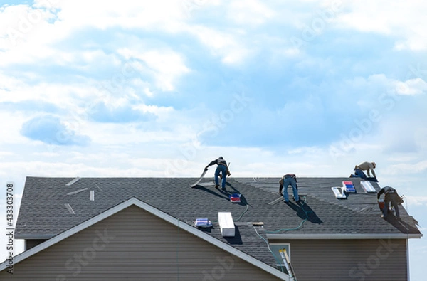 Fototapeta 4 construction workers fixing roof against clouds blue sky, install shingles at the top of the house. Renovate, improvement, build home exterior by professional teamwork. Safety and protection concept