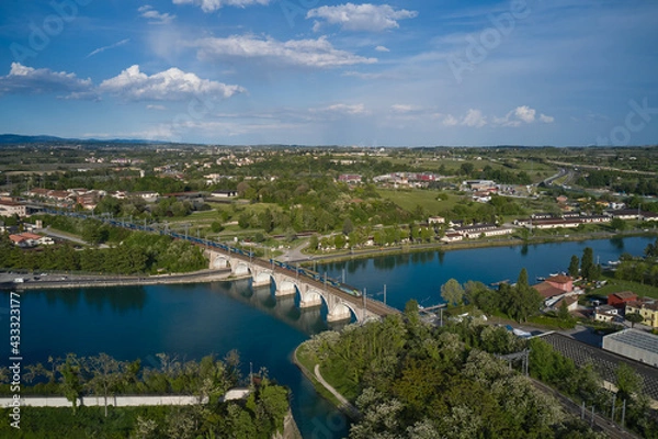 Obraz Panoramic aerial view of the train passing over the railway bridge over the river. Peschiera del Garda, Italy. Aerial view of the resort town on Lake Garda.