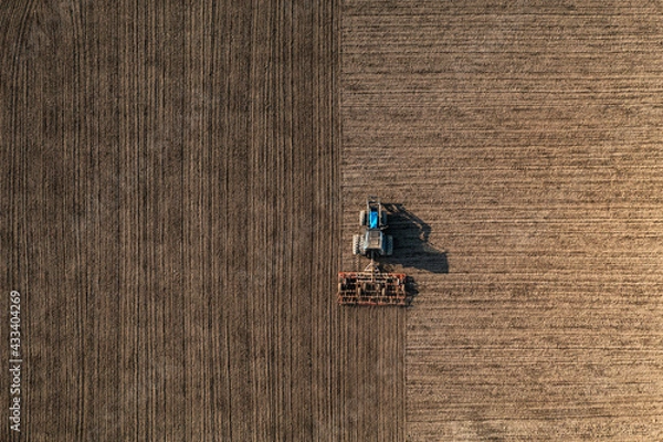 Fototapeta Top view of a tractor harrowing soil on an agriculture field. Acricultural tillage or land preparation.