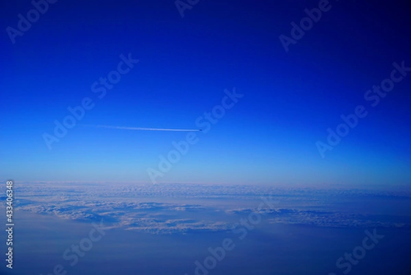 Obraz 一面の雲海の上を長い飛行機雲を引きながら遠くを飛ぶジェット機