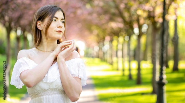 Fototapeta Dreamy young brunette in a bright summer park.