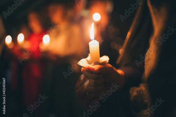 Fototapeta a girl holds a lighted candle in her hands, a religious tradition, a symbol of the Christian faith, a wax candle burns with an even flame, blow out a candle, a smoke from an extinguished wick