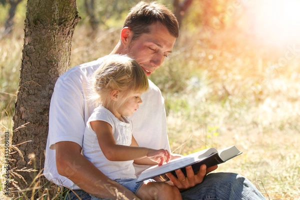 Fototapeta Happy parents with a child read the Bible in the nature park