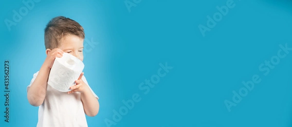 Obraz A little boy gently holds in his hand roll of toilet paper on blue background, banner. The buying toilet paper concept