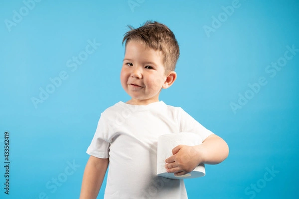 Obraz A little boy gently holds in his hand roll of toilet paper on blue background. The buying toilet paper concept