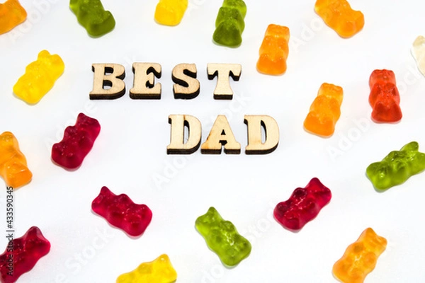 Obraz Text in wooden letters: best dad, with scattered colourful gummy bears isolated on white background, flat lay
