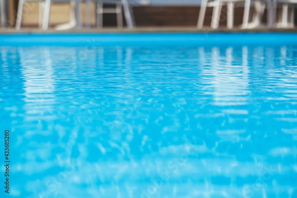 Fototapeta Pool with blue ripped water and wooden deck at tropical resort in sunny light.  Swimming pool surface with space for text. Summer vacation and relax. Travel