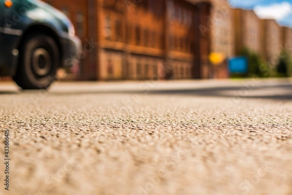 Fototapeta Summer in the city, the empty street and passing car.  Close up view from the asphalt level
