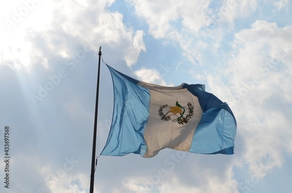 Fototapeta Bandera de Guatemala ondeando en el cielo cubierto de nubes a la luz del día