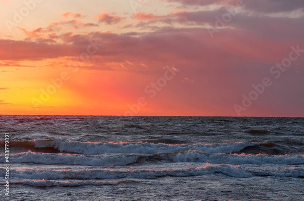 Obraz Stunning sunset reflections on the crashing sea waves. Red and orange background and light clouds.