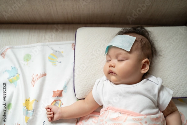 Fototapeta asian baby infant get fever and apply cool patch on forehead sleeping at home after vaccination. cold pad gel healing temperature. baby sick after back from hospital.