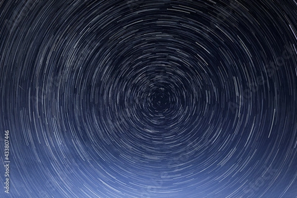 Fototapeta Stellar trails, the rotation of bright stars at night around the Polar Star against a blue sky and a meteor