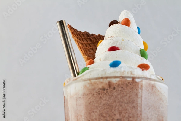 Obraz Sundae visto desde frente, con crema batida, rockets ,una bombilla y un trozo de cucurucho sobre un fondo blanco