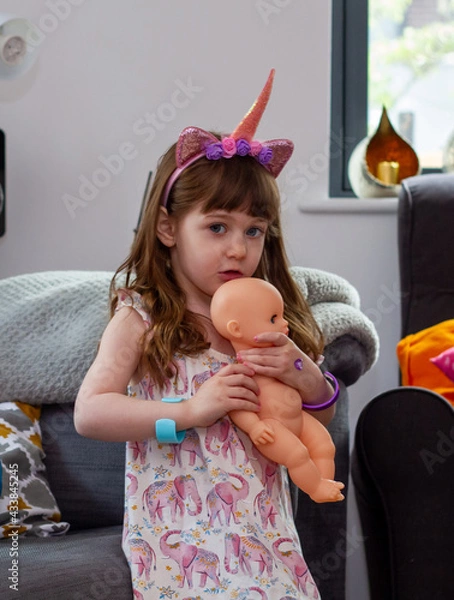 Obraz A Cute Baby Girl Sitting On A Sofa With A Doll