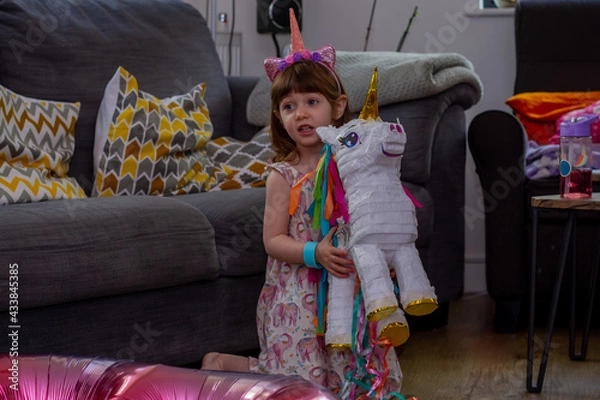 Obraz A Cute Baby Girl Sitting On The Floor With a Balloon And An Unicorn Pinata