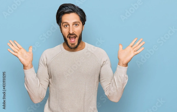Fototapeta Young hispanic man wearing casual clothes celebrating victory with happy smile and winner expression with raised hands