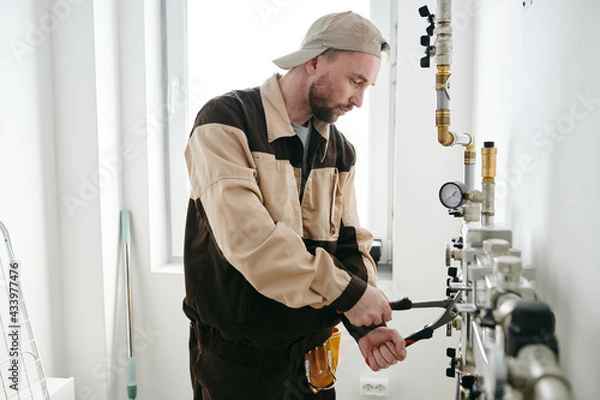 Obraz Young plumber using handtools during repair work in bathroom or toilet