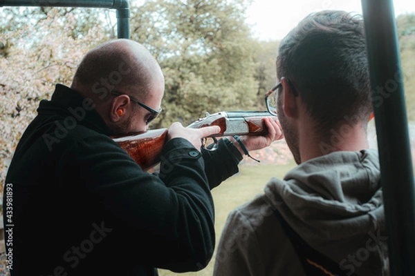Fototapeta Two men practicing clay shooting. One teaching the other newbie the ropes. Cold winter day in the UK