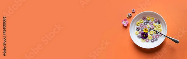 Fototapeta on a peach plain background a beautiful summer American breakfast: multi-colored flakes rings with milk and violet flowers of yellow pink and violet color. there is a spoon in the plate