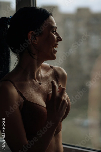 Obraz A silhouette of a smiling brunette girl who stands at the window in her lingerie and sprinkles perfume on herself