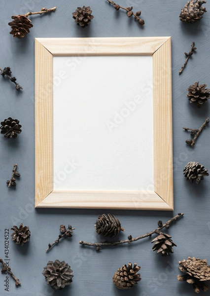 Fototapeta Forest vacation stationery mock-up scene. Blank white greeting card in wooden frame surrounded by cones on textured gray background.