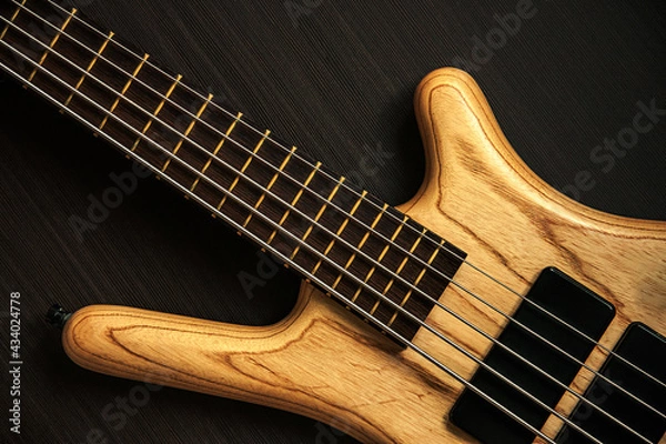 Obraz Close up of electric bass guitar with five strings. Detailed view of wooden varnished texture of musical instrument on dark brown background. Music classes, concert, hobby and bass player concept 