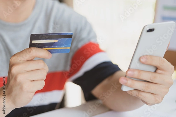 Fototapeta Man using smartphone and mock up credit card for shopping online. Pays for purchase.Online payment,buy and sell products & services.