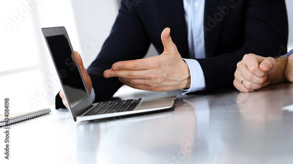 Obraz Business people using laptop computer while working together at the desk in modern office. Unknown businessman or male entrepreneur with colleague at workplace. Teamwork and partnership concept