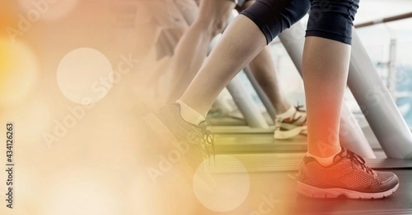 Fototapeta Composition of woman running on treadmill with red spot on ankle and spots of light